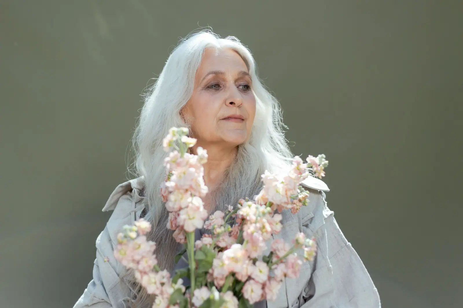 A resident with long silver hair holding a spray of white spring blossoms against a soft green wall