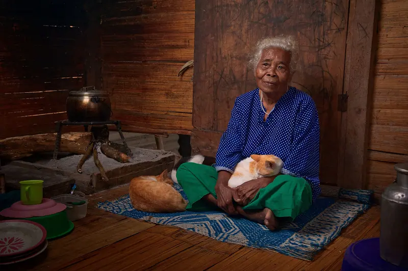 A resident sitting on a rug by the stove with a cat in her lap