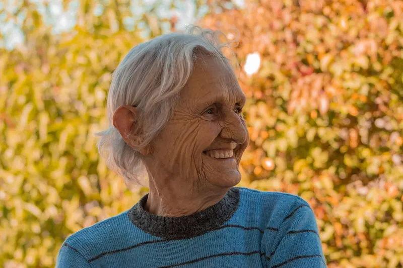 A resident smiling among the yellow autumn leaves