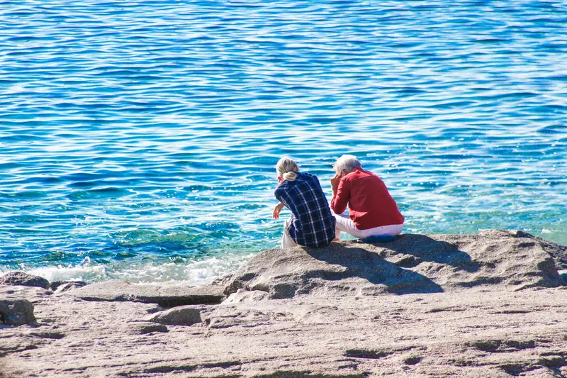 A couple sitting on the rocks above the blue water