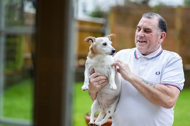 A resident laughing as he holds up the little white terrier
