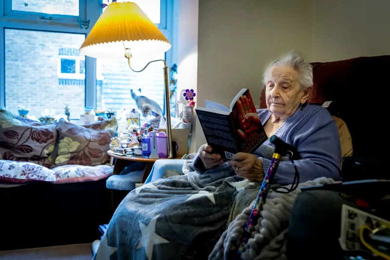 A resident reading in her armchair under a yellow lamp