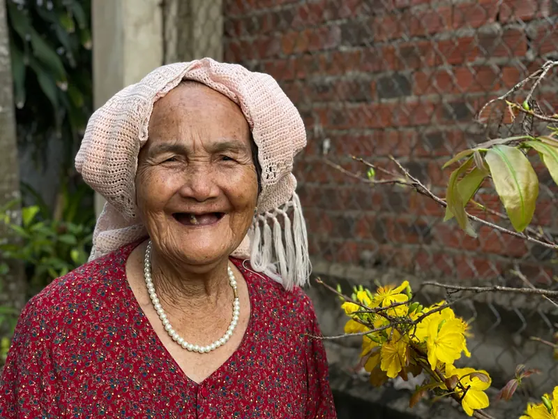 A smiling resident in a pink headscarf and pearls by the garden wall