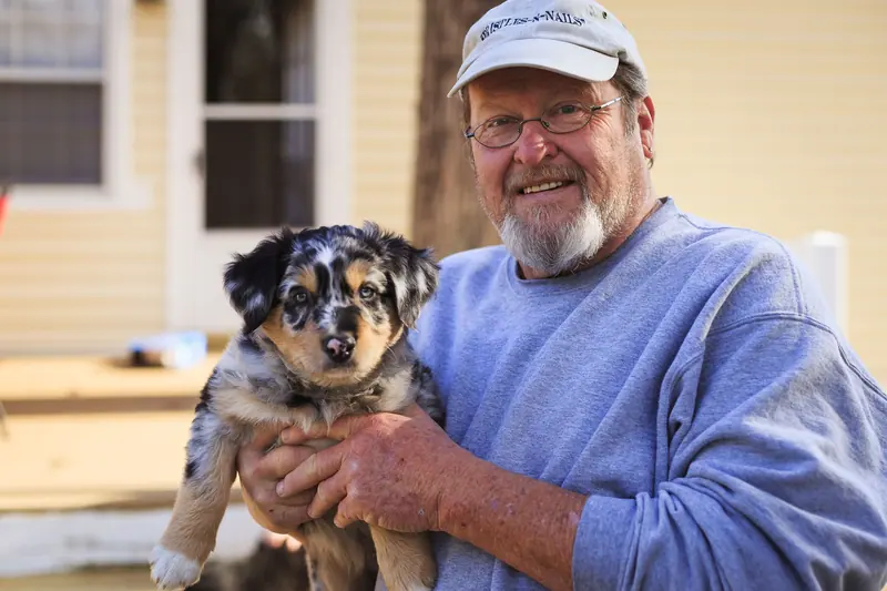 A resident in a ball cap holding a speckled puppy
