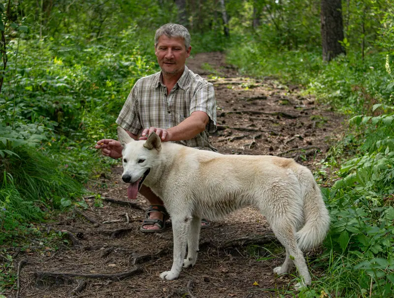 A resident walking a white dog along the wooded trail
