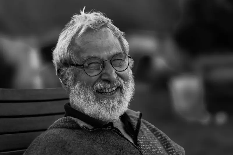 Portrait of a resident with a white beard and round glasses, laughing
