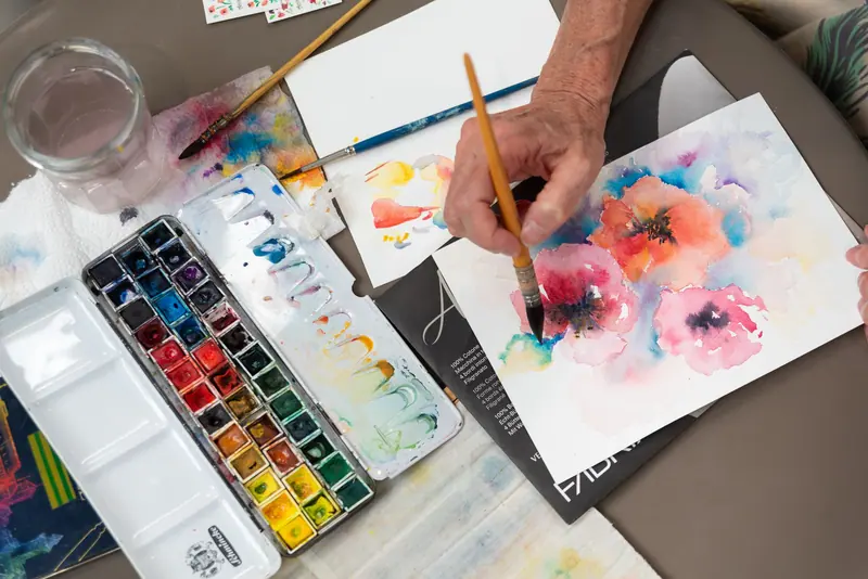 A resident's hand painting a watercolor of pink poppies