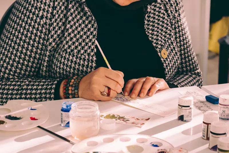 A resident painting a ceramic tile with a fine brush