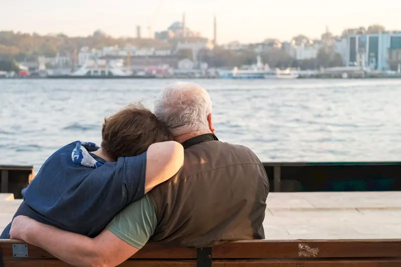 A couple with their arms around each other on a waterfront bench