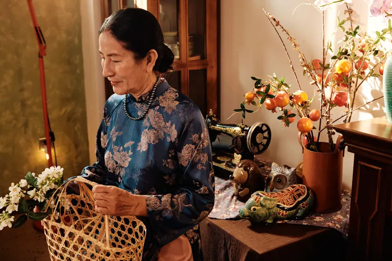A resident in a blue silk áo dài arranging white blossoms beside her sewing machine