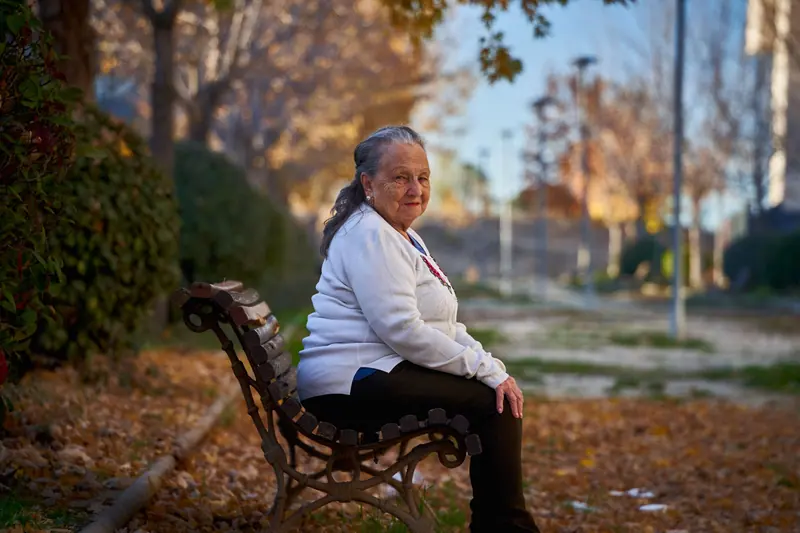 A resident on a park bench among fallen leaves