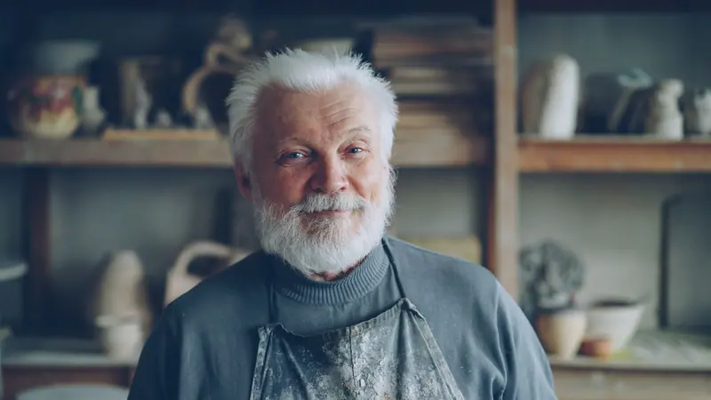 Portrait of a resident with a white beard among shelves of pottery