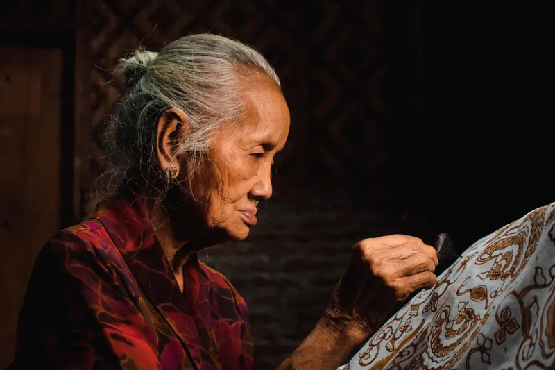 A resident embroidering a pattern by lamplight