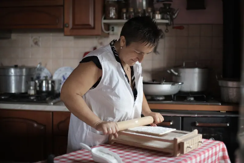 A resident rolling out dough on a checkered tablecloth