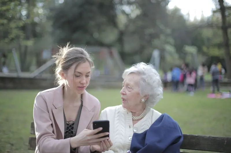 A student showing a resident photos on her phone in the park