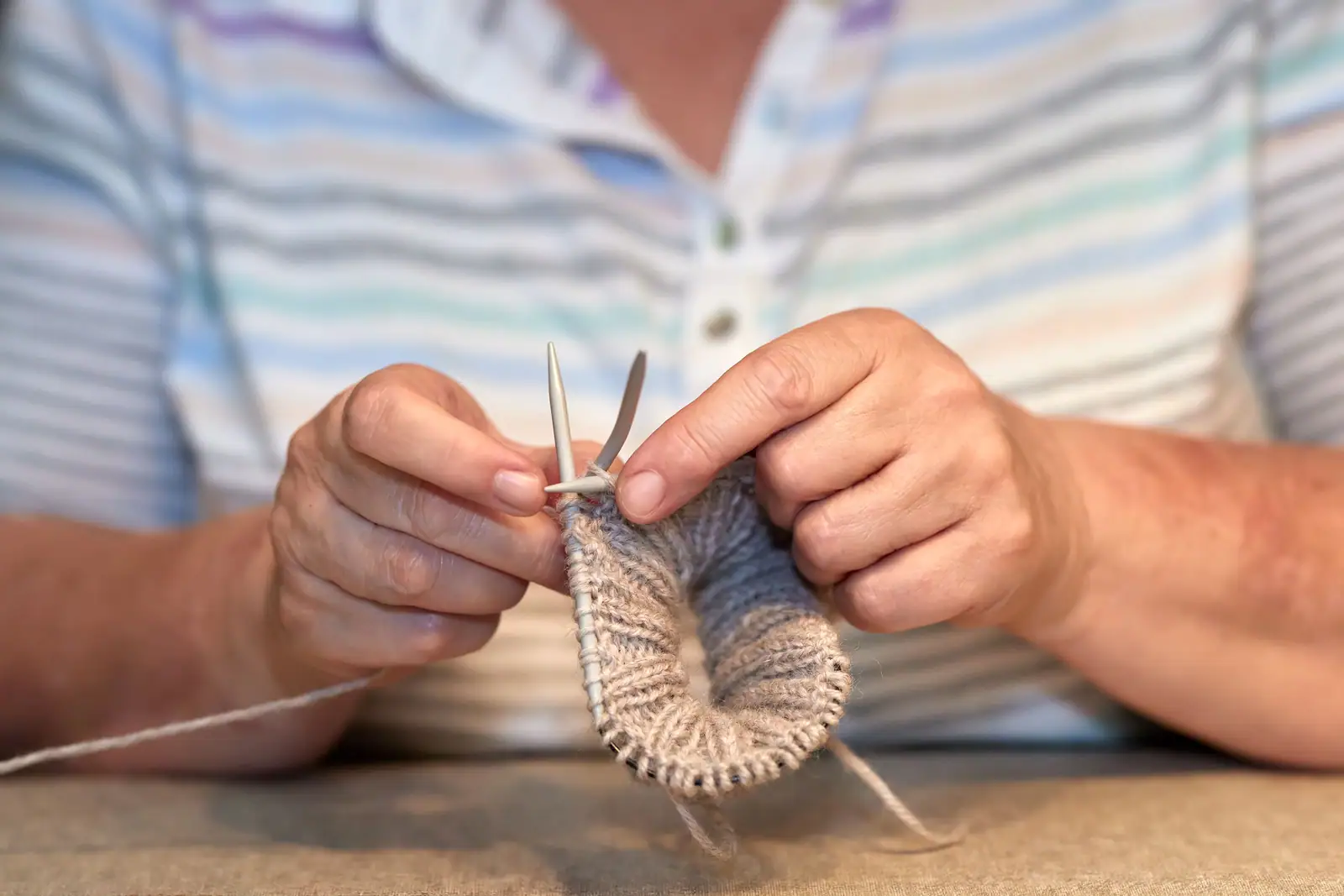 A resident's hands knitting a gray sock on four needles
