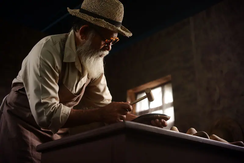 A resident in a straw hat leaning over his workbench in low light