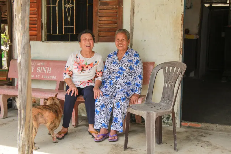 Two residents laughing on the porch bench with the house dog