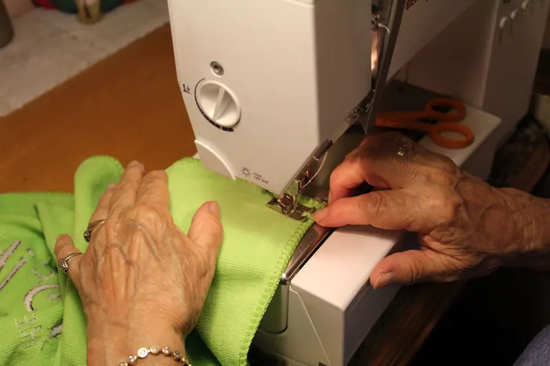 Fingers guiding green fabric through the machine