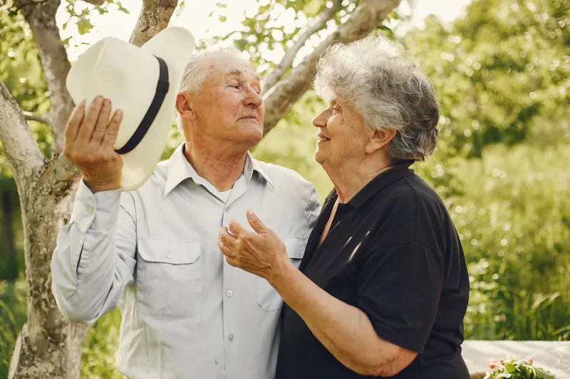 A resident and her husband laughing in the garden in their sun hats