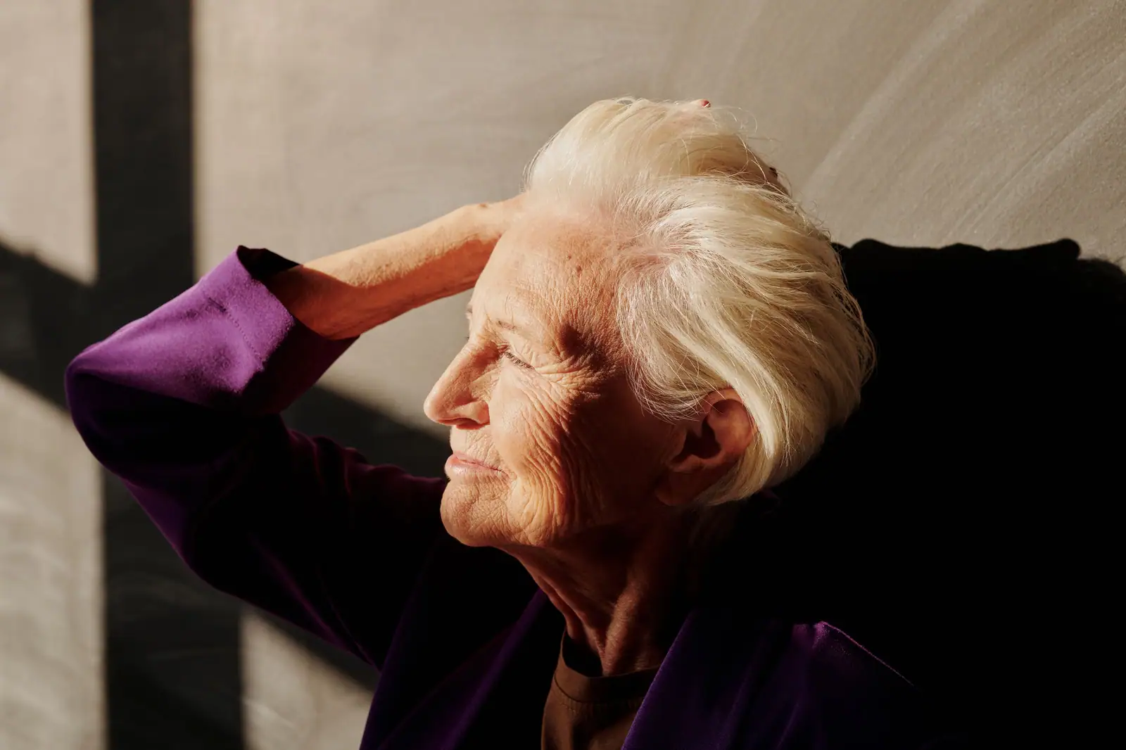 Captivating portrait of a smiling senior woman with gray hair enjoying sunlight indoors.