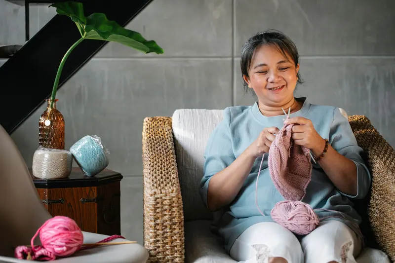 A resident knitting in a wicker chair by the window
