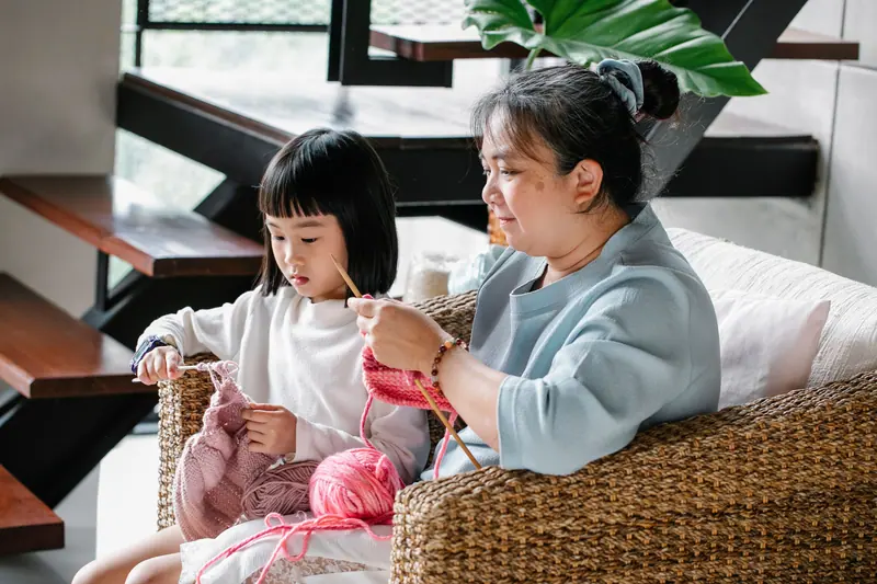 A resident and a girl knitting side by side