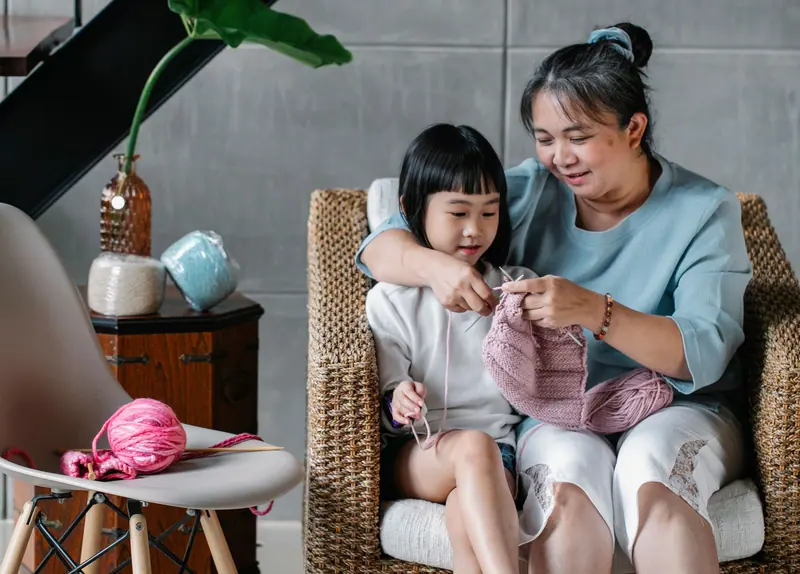 A resident teaching a girl to knit in the sunroom