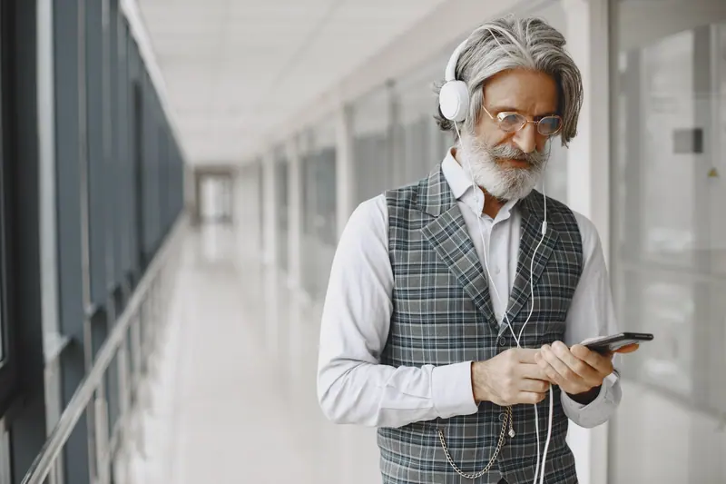 A resident in a plaid vest listening to music in the bright hallway