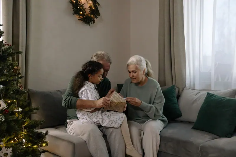 A resident and her granddaughter opening presents by the tree