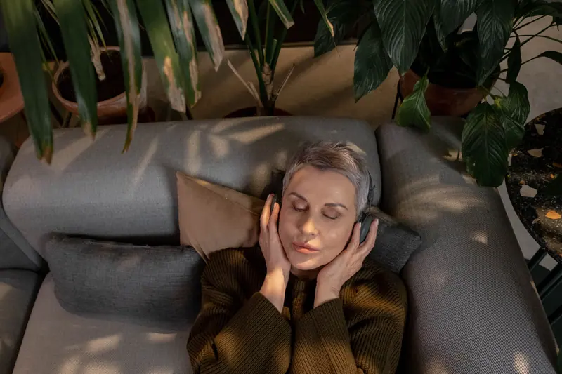 A resident lying back on the sofa with headphones and her eyes closed