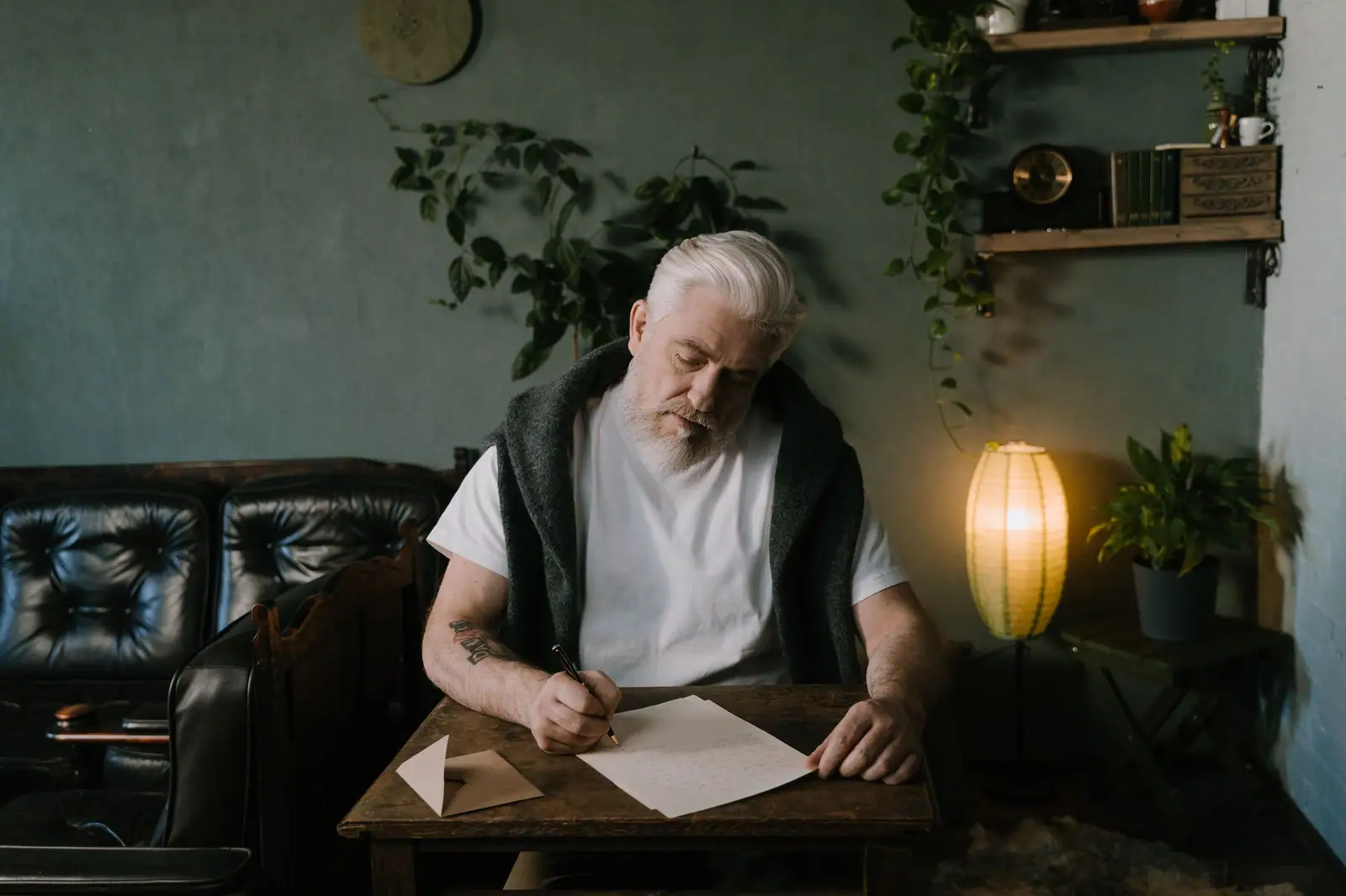 A resident in a white T-shirt writing a letter at a low wooden table under a glowing paper lantern