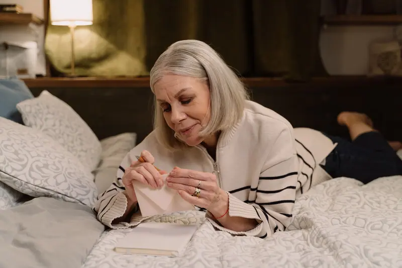 A resident addressing an envelope on her bed in the lamplight