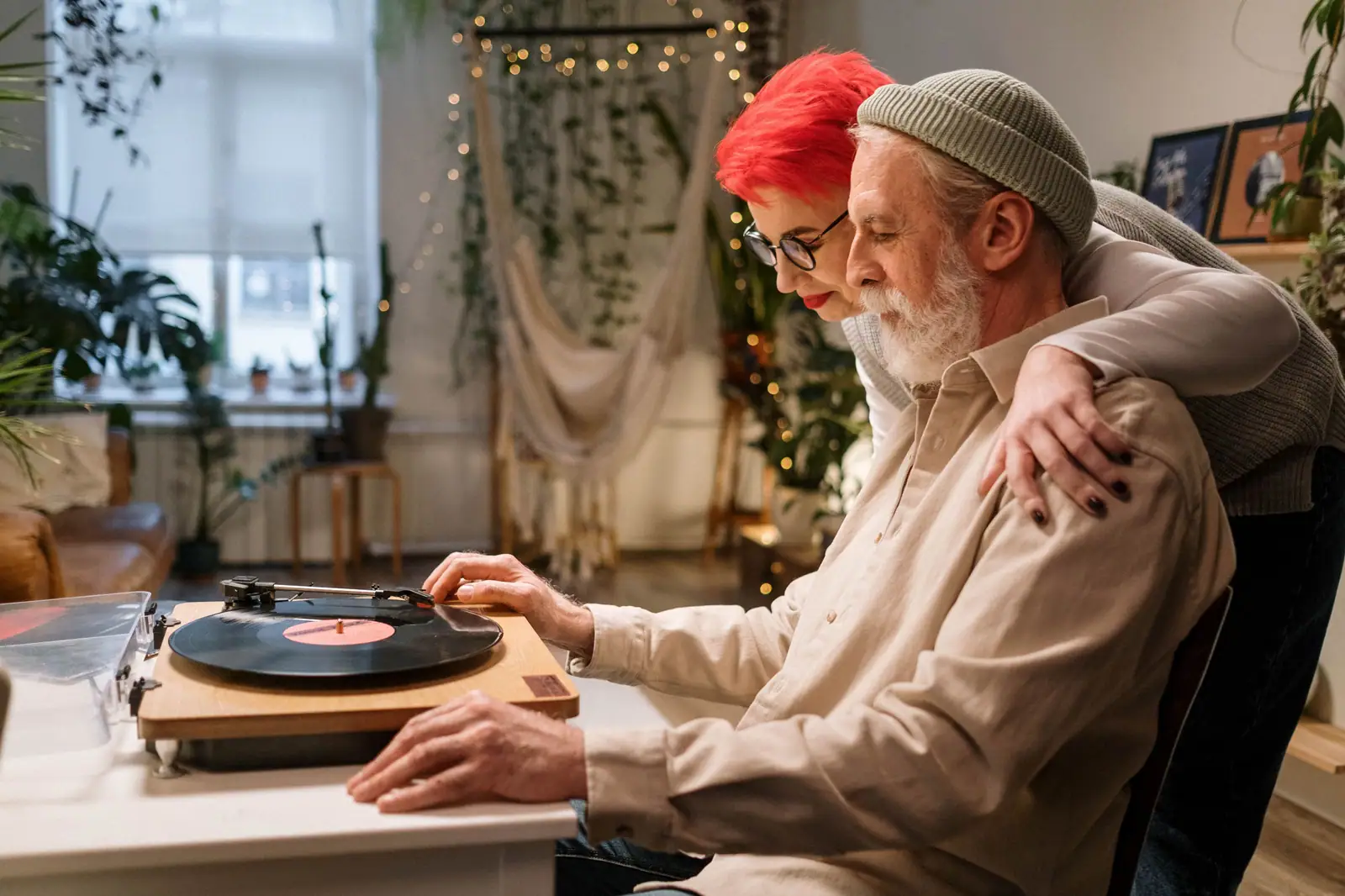 A resident at the record player while his daughter leans over his shoulder in the lamplit parlor