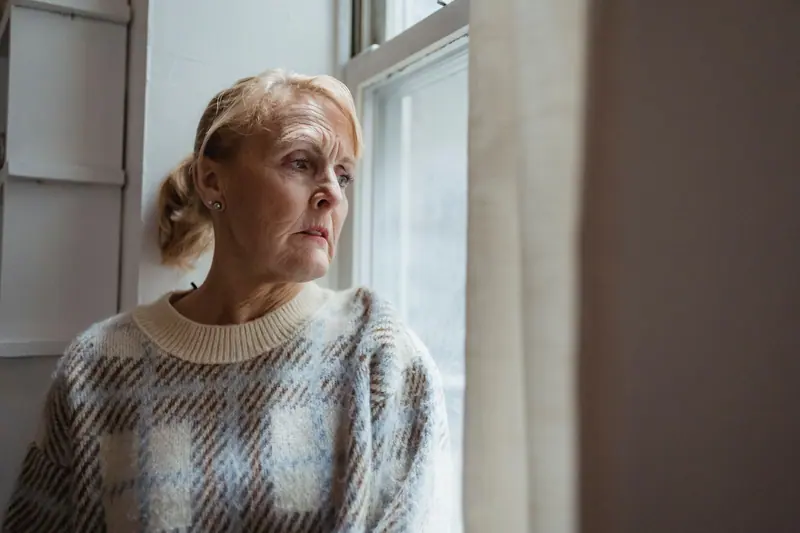 A resident in a wool sweater looking out the window