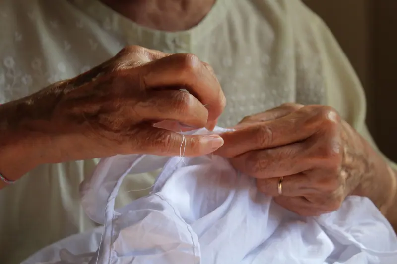 A resident's hands stitching white fabric