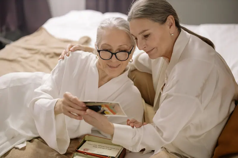 A resident and her daughter laughing over a stack of old photographs