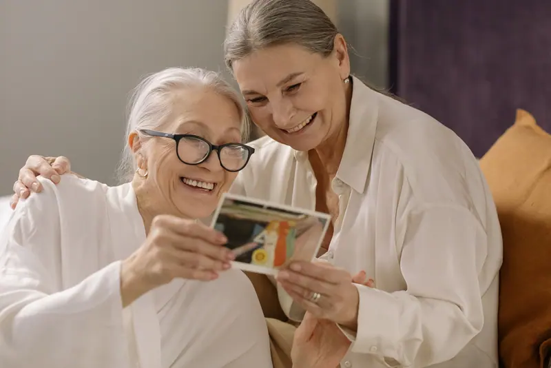 A resident and her caregiver smiling over an old family photograph