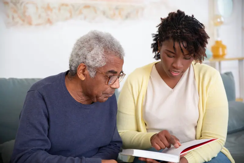 A student volunteer reading with a resident on the sofa