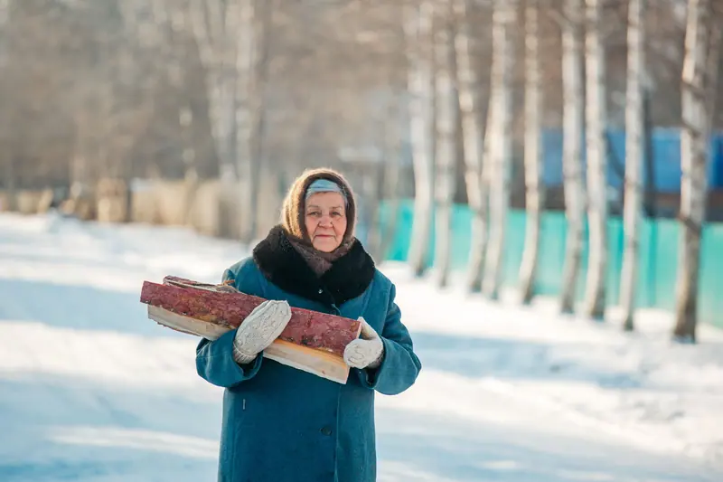 A resident in a teal coat with an armful of logs