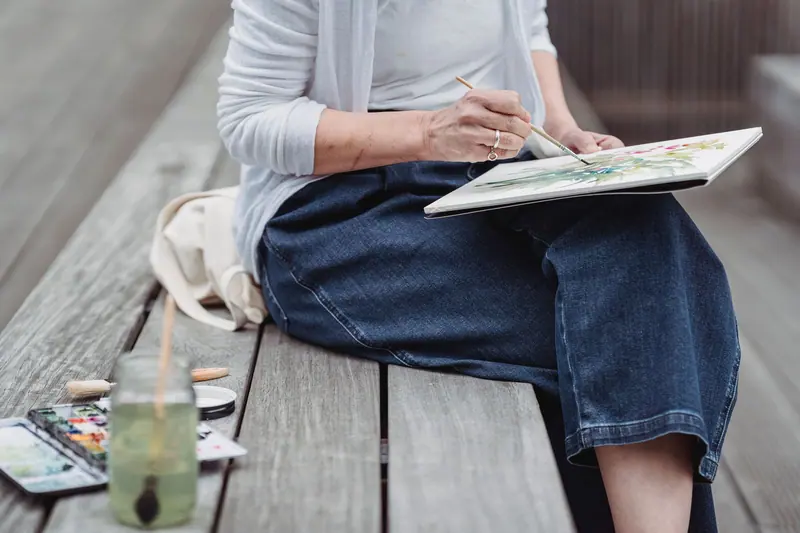 A resident painting on a board balanced on her knee