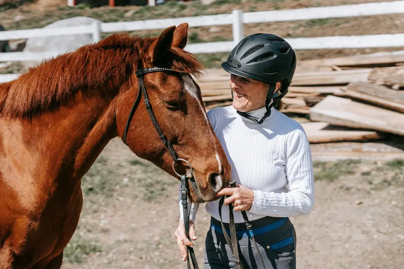 A visitor in a riding helmet leading a pony across the yard
