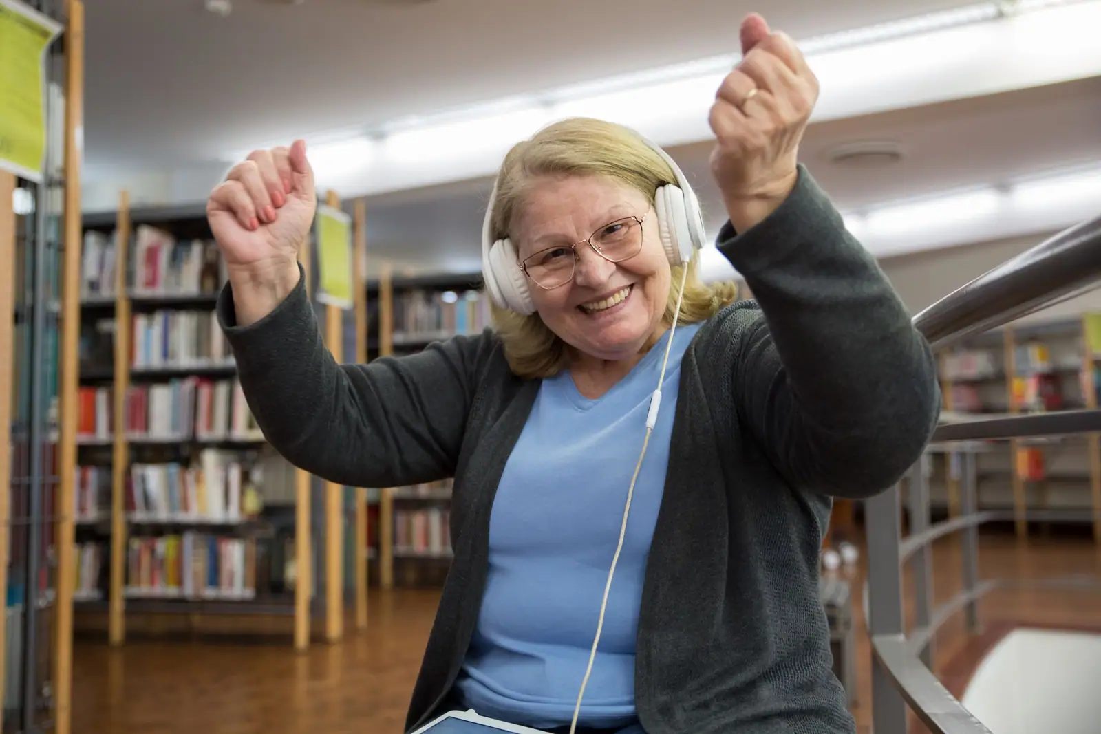 A resident in headphones dancing with both fists up between the library shelves