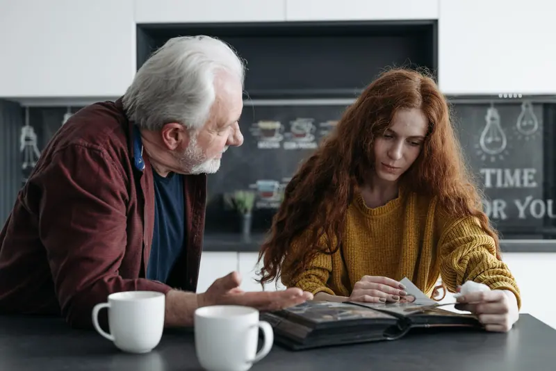 A resident and a young volunteer looking at a photo album with coffee