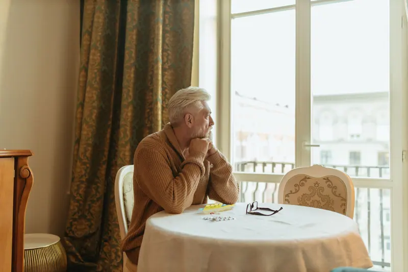 A resident sitting at a small round table by the window in the afternoon light