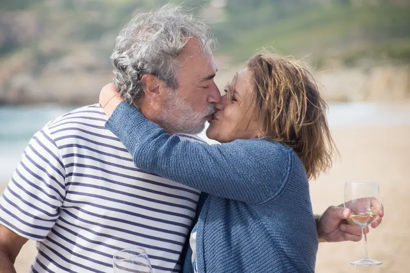 A couple kissing on the beach, a glass of wine in her hand