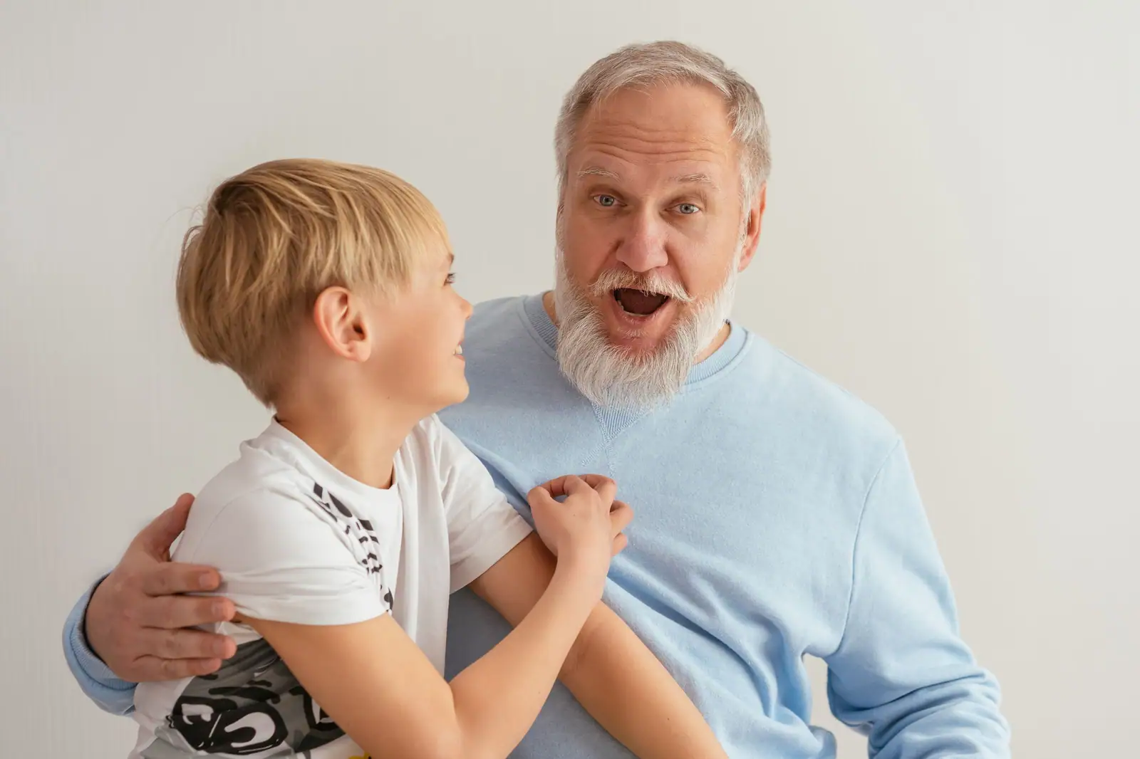 A resident in a blue sweater making a surprised face for a laughing preschooler