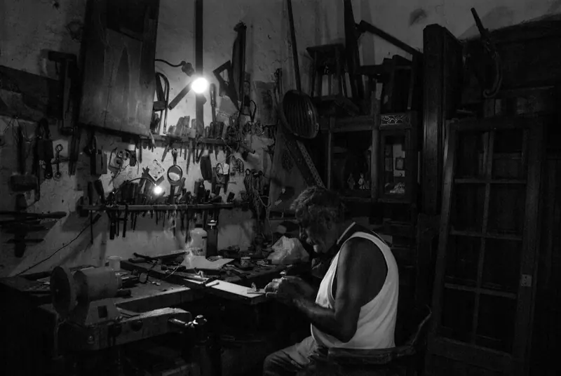 A resident working at a cluttered workbench under a single lamp