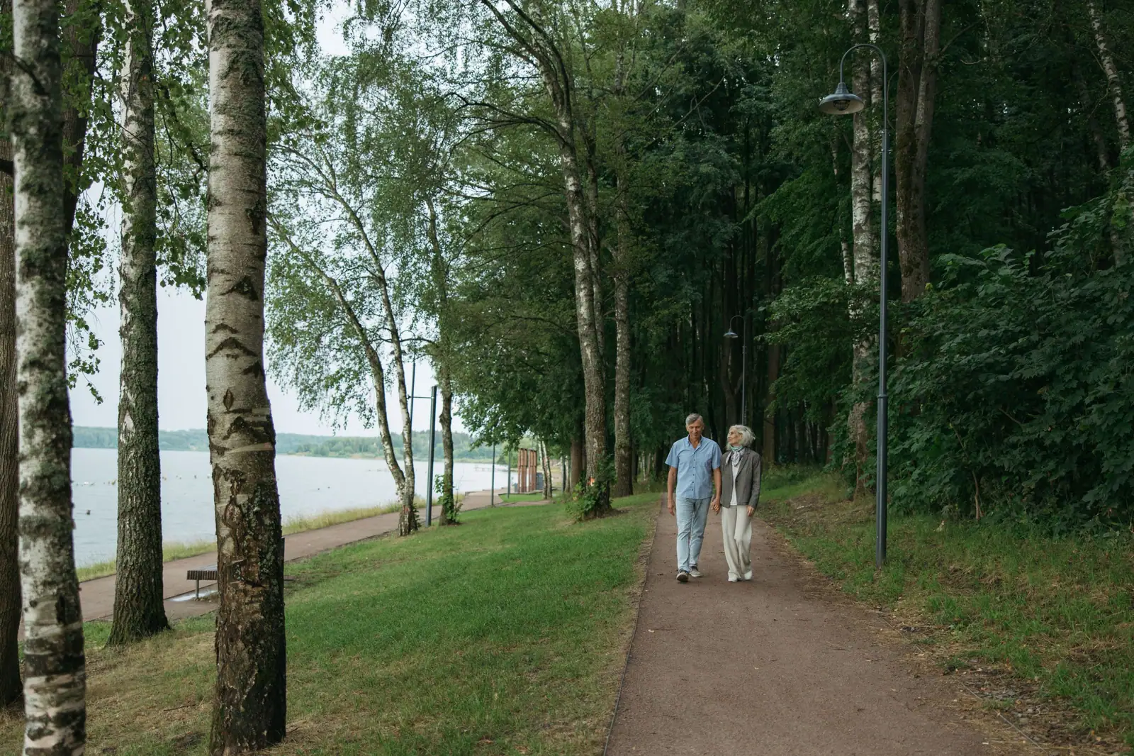 A senior couple enjoys a peaceful walk along a tree-lined path in a serene park setting.