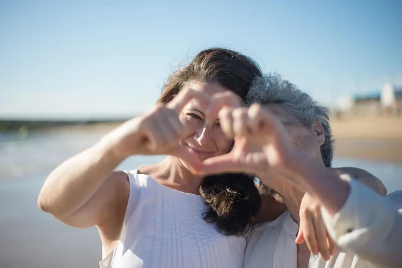 A mother and daughter making a heart with their hands on the beach